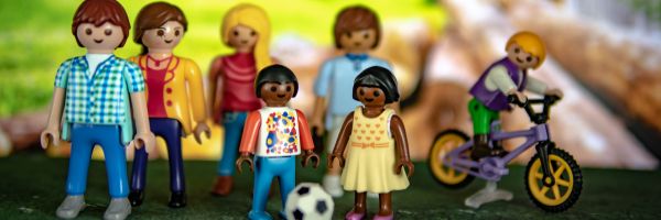 03-	Eine Gruppe Playmobilfiguren steht zusammen, ein Kind sitzt auf einem Fahrrad, ein anderes spielt Fußball.