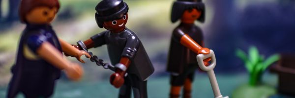 Eine Playmobilfigur ist in Ketten, eine weitere hält eine Schaufel, sie werden von einer dritten Figur bewacht.