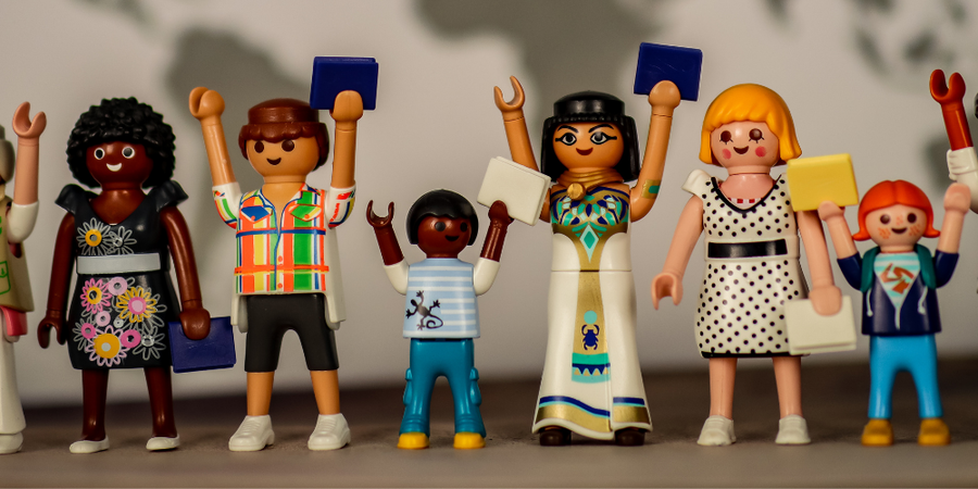 14- Eine Gruppe asylsuchender Playmobilfiguren sitzt in einem Lager.