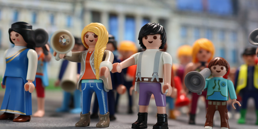 19- Eine Gruppe Playmobilfiguren steht zusammen, eine von ihnen spricht in ein Megafon.