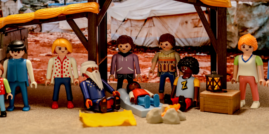 14-	Eine Gruppe asylsuchender Playmobilfiguren sitzt in einem Lager.